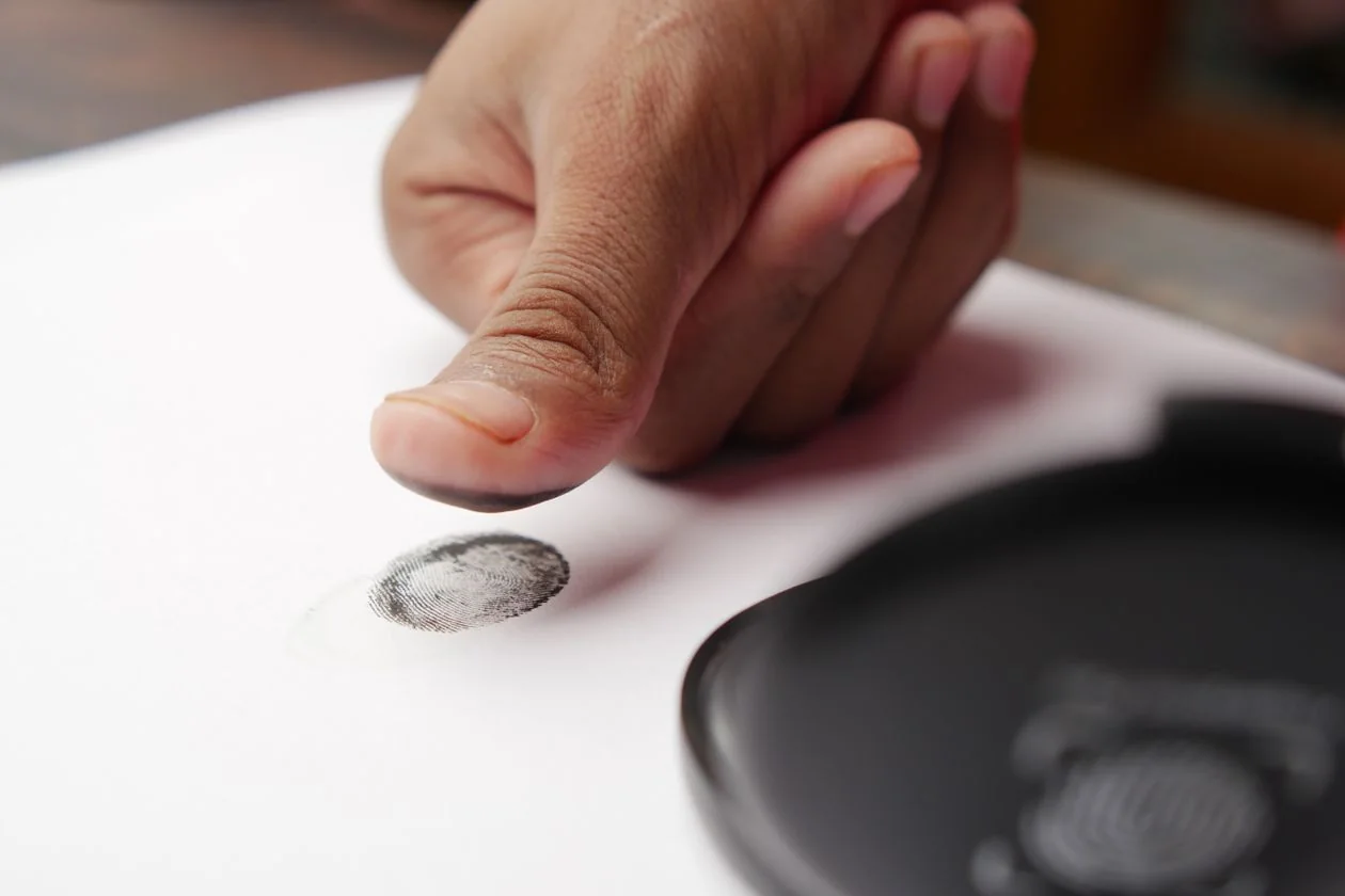 A close-up of a thumb pressing an ink fingerprint onto a registration paper during biometric verification.