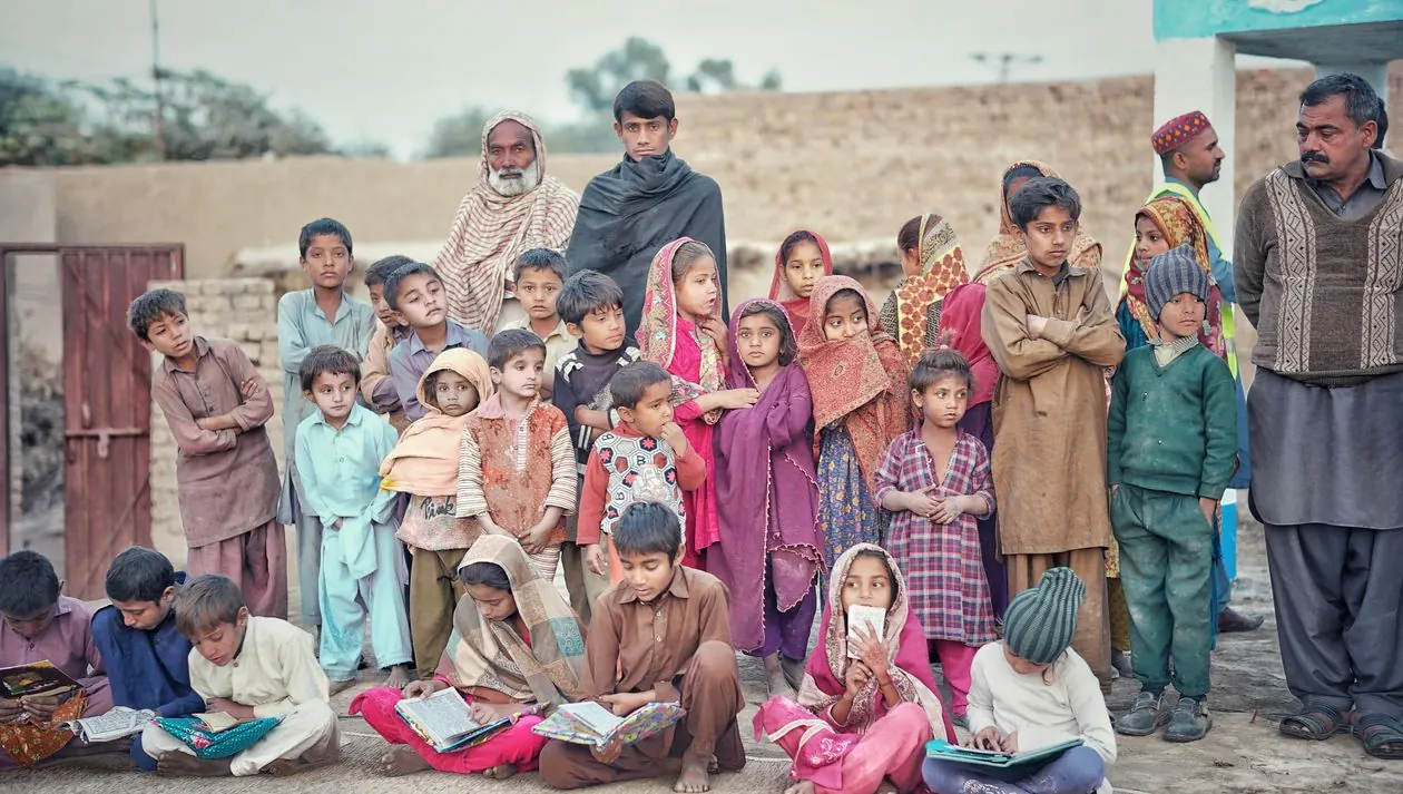 Pakistani village children sitting on the ground with their school books during an outdoor lesson.
