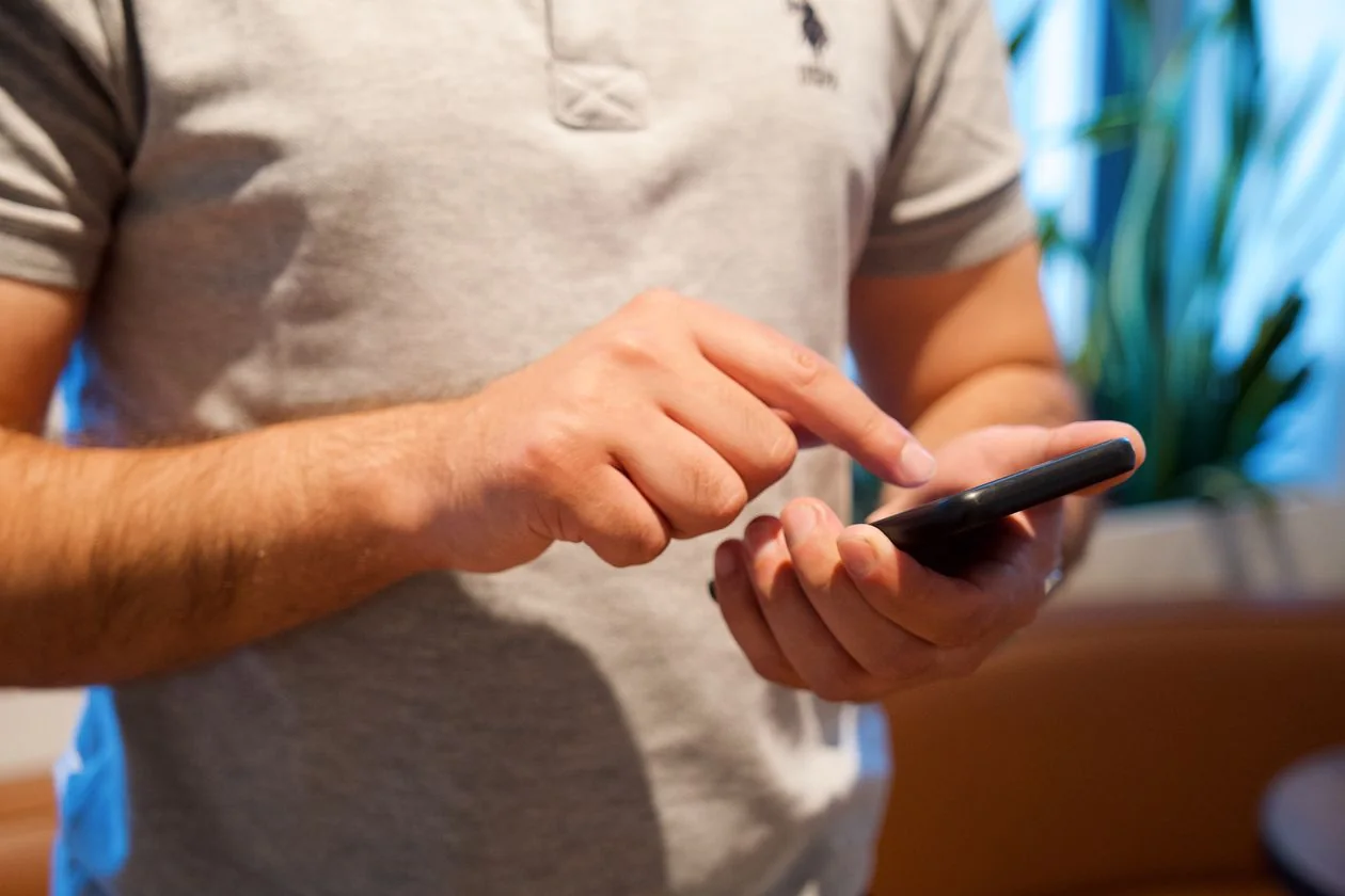 A man tapping on his smartphone screen indoors while checking a message.