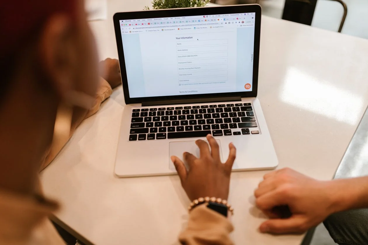 Two people filling an online application form together on a laptop