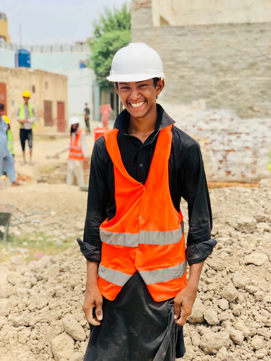 A smiling young construction worker in a helmet and safety vest at a building site in Punjab