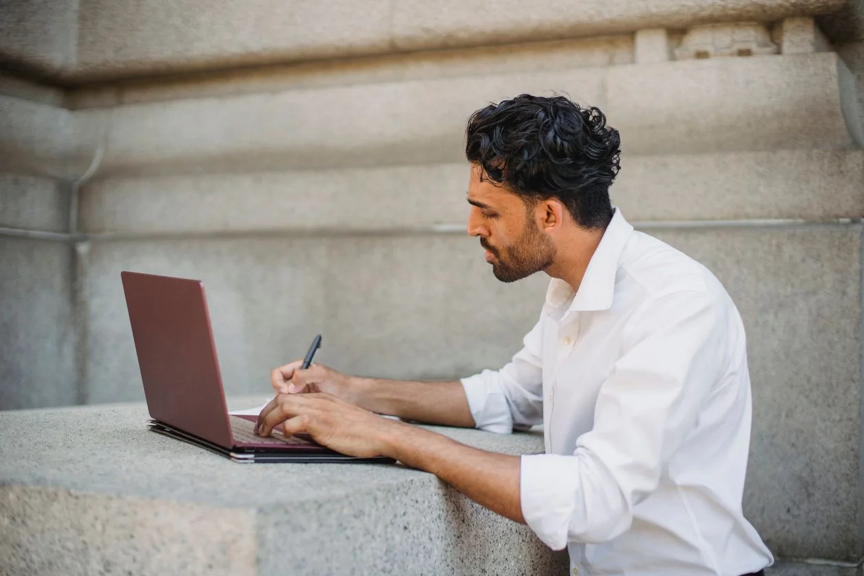 A man calmly working through an application on his laptop with a pen and notes