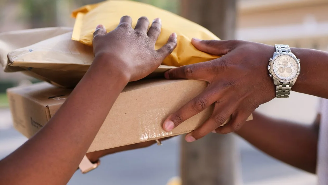 Hands passing a stack of parcels and envelopes from one person to another during a delivery.