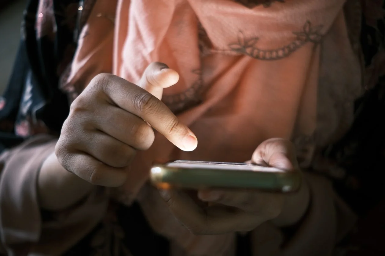 A woman in a peach dupatta tapping on her smartphone to send an SMS.
