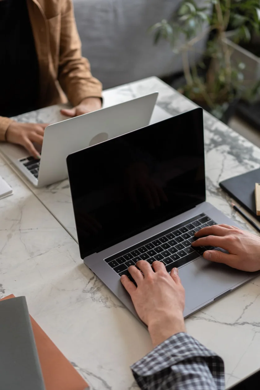 Two people typing on laptops at a clean marble desk while working online.