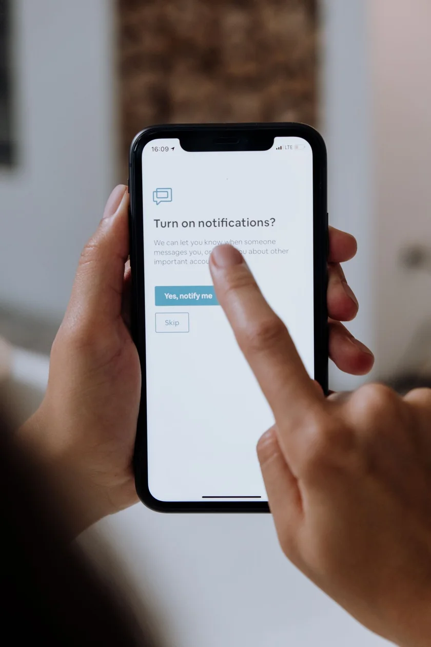 A person holding a smartphone showing a notifications prompt in a mobile app.